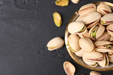 Tasty pistachios in bowl on black table, top view. Space for text