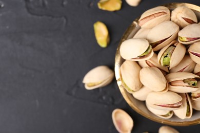 Photo of Tasty pistachios in bowl on black table, top view. Space for text