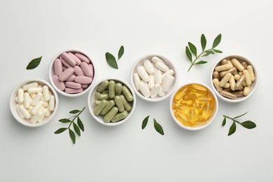 Photo of Different vitamin capsules in bowls and leaves on white background, flat lay