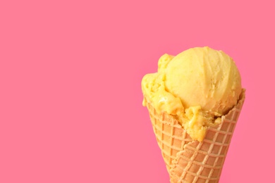 Photo of Delicious yellow ice cream in waffle cone on pink background, closeup. Space for text