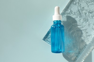 Bottle of cosmetic serum on light blue background, top view. Space for text