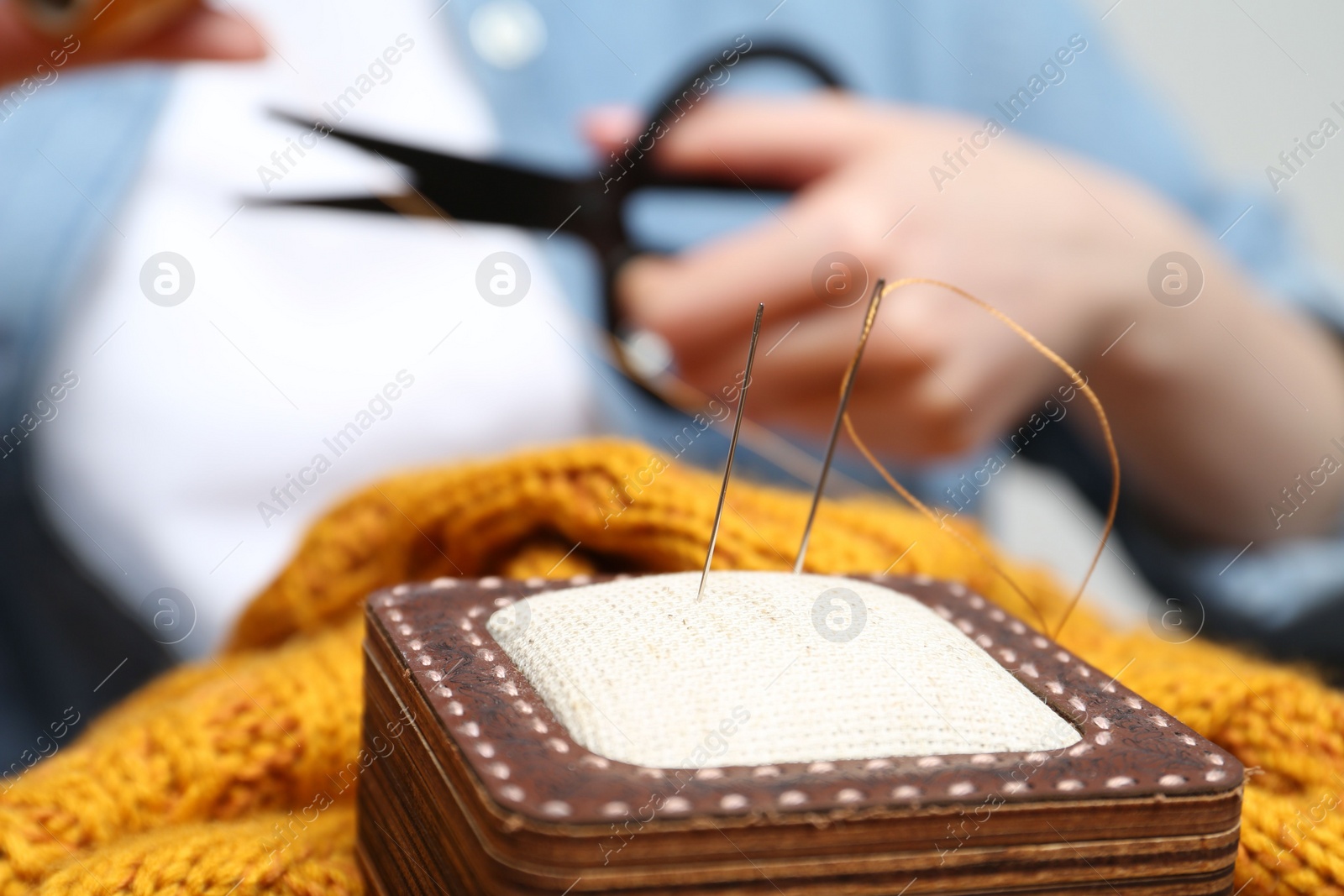 Photo of Woman sewing sweater, focus on pin cushion