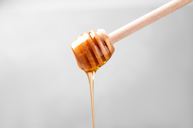 Pouring tasty honey from dipper on light grey background, closeup