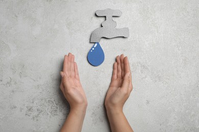 Photo of Save Water concept. Woman at light grey table with paper tap and drop, top view