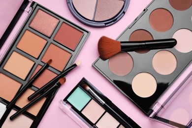Photo of Colorful contouring palettes with brushes on pale pink background, flat lay. Professional cosmetic product