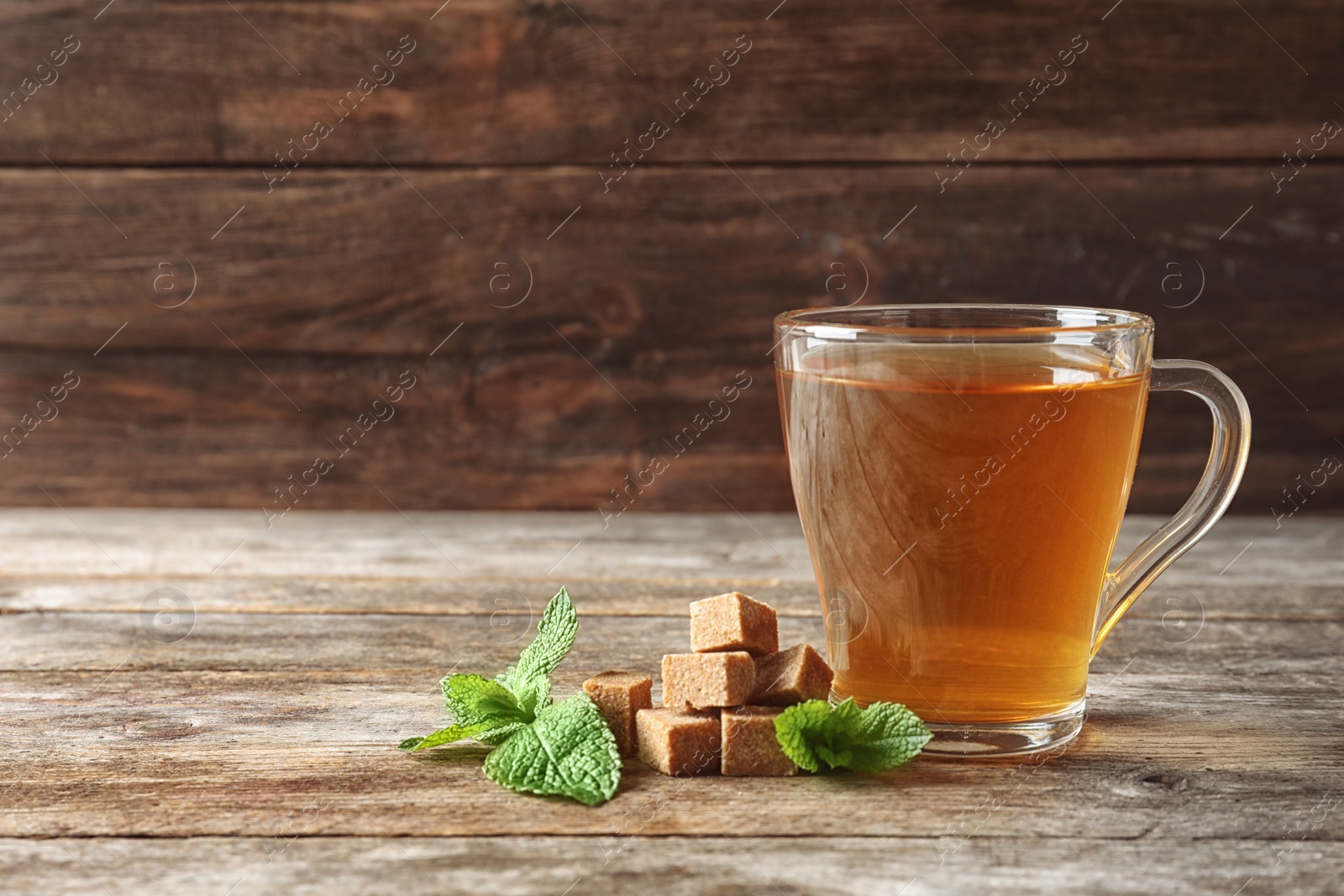 Photo of Cup with hot aromatic mint tea, fresh leaves and sugar cubes on wooden table