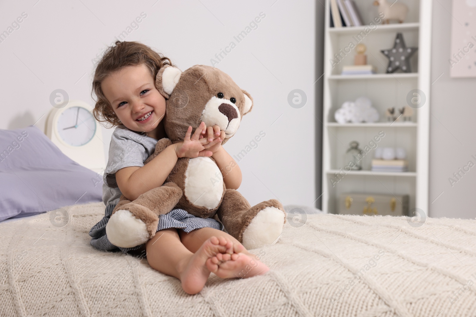 Photo of Cute little girl with teddy bear on bed at home