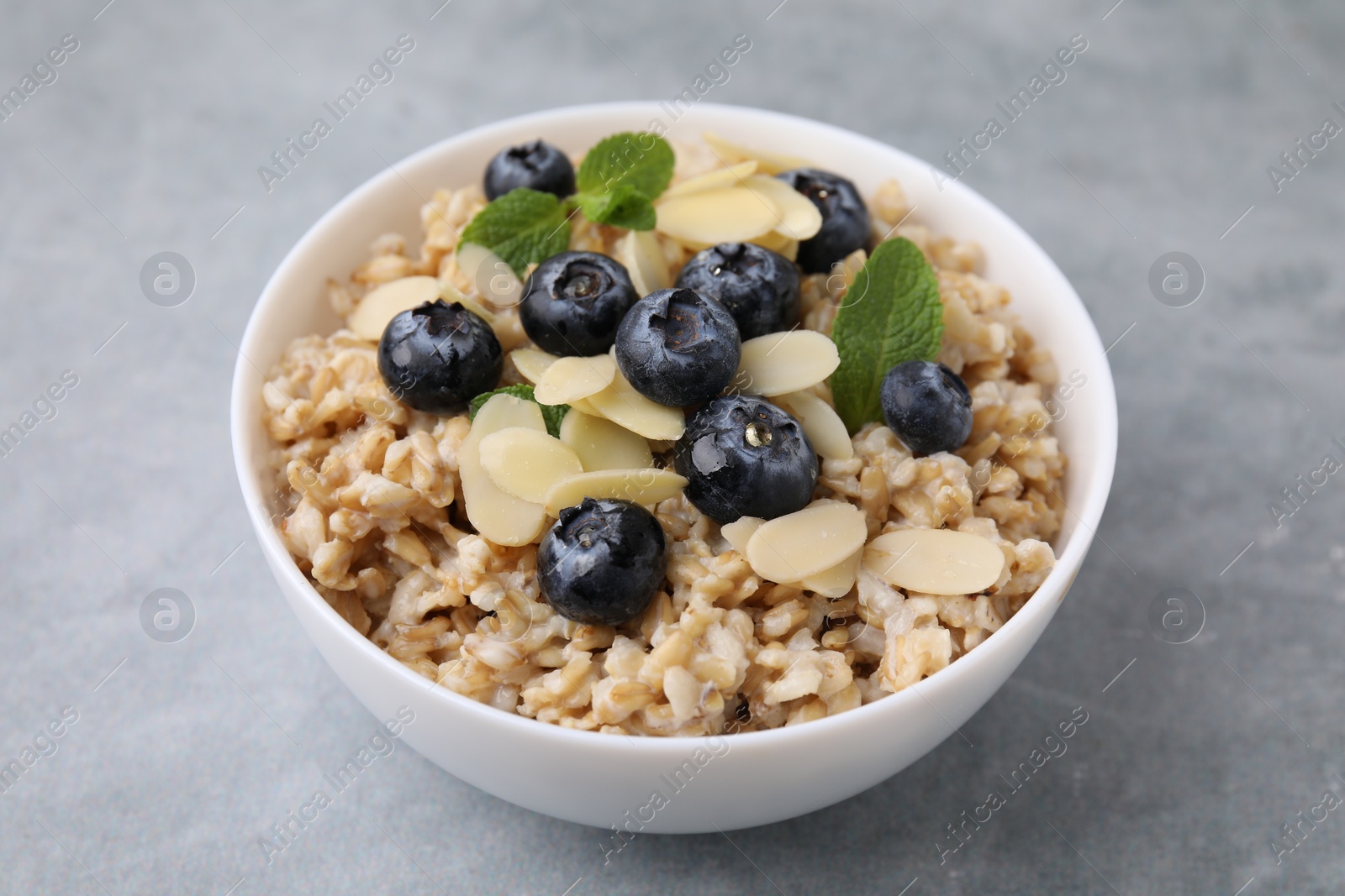 Photo of Tasty oatmeal with blueberries, mint and almond petals in bowl on grey table