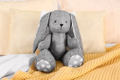 Photo of Cute stuffed toy rabbit on comfortable bed in child's room interior