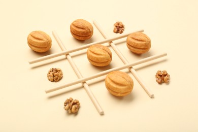 Photo of Tic tac toe game made with walnuts and cookies on beige background