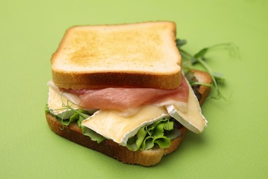 Photo of Tasty sandwich with brie cheese and prosciutto on light green background, closeup