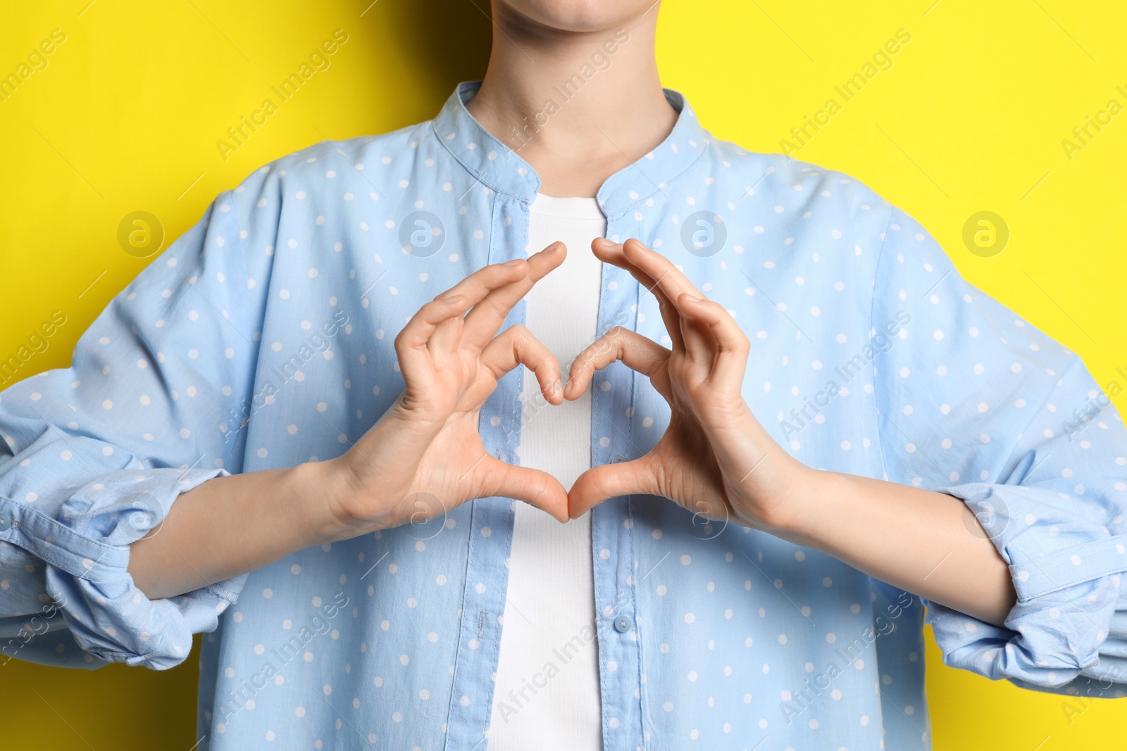 Photo of Woman making heart with hands on yellow background, closeup