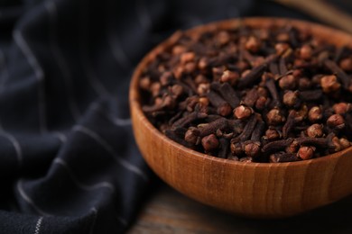 Photo of Aromatic cloves in bowl on wooden table, closeup. Space for text