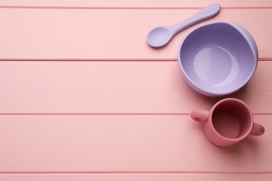 Set of plastic dishware on pink wooden background, flat lay with space for text. Serving baby food