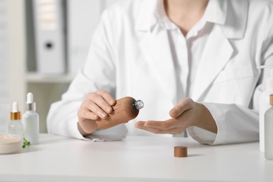 Photo of Dermatologist with bottle testing cosmetic product at white table indoors, selective focus