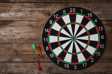 Dart board with color arrows on wooden background, top view. Space for text