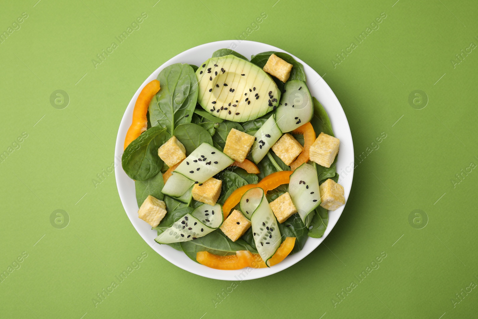 Photo of Bowl of tasty salad with tofu and vegetables on green background, top view