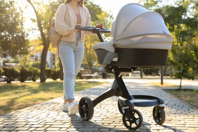 Photo of Young mother walking with her baby in stroller at park on sunny day, closeup