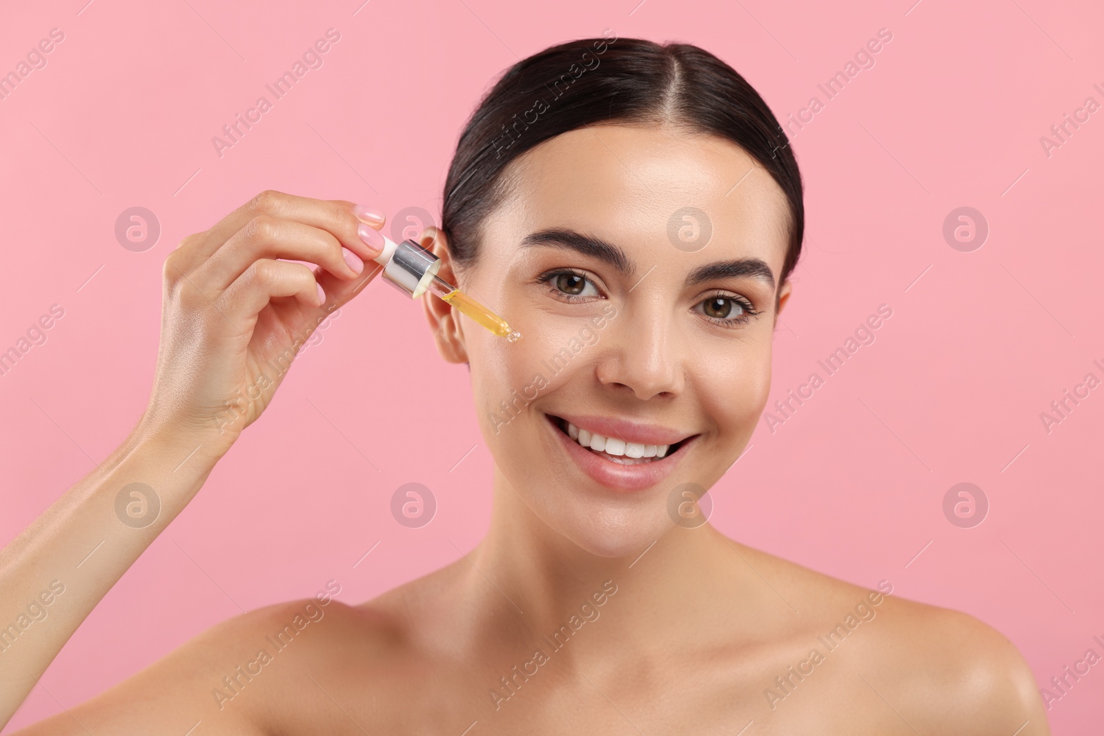 Photo of Beautiful young woman applying serum onto her face on pink background