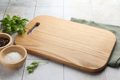 Photo of Cutting board, salt, pepper and parsley on white tiled table. Space for text