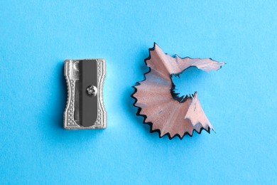 Photo of Metal sharpener and pencil shavings on light blue background, flat lay