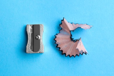 Metal sharpener and pencil shavings on light blue background, flat lay