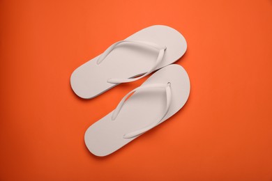 Stylish white flip flops on orange background, top view