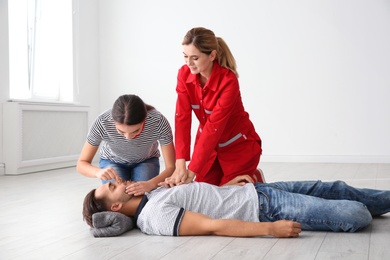 Instructor with woman practicing first aid on unconscious man indoors