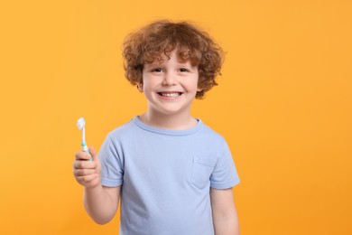 Photo of Cute little boy holding plastic toothbrush on yellow background