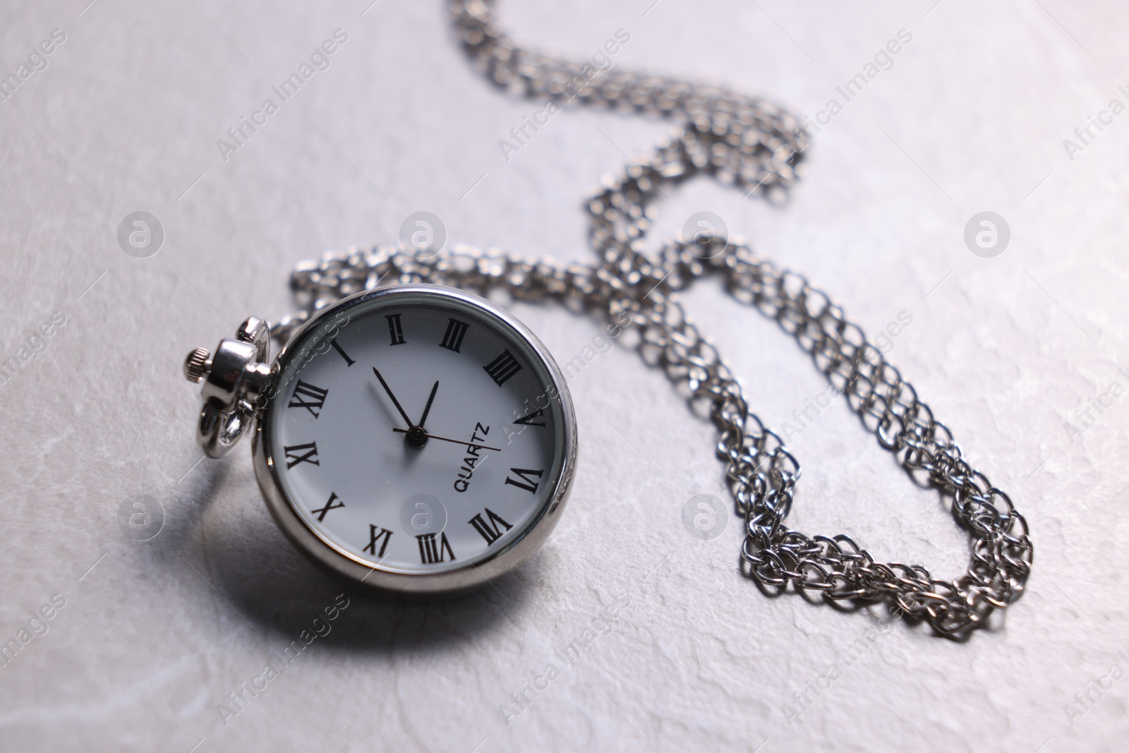 Photo of Silver pocket clock with chain on light textured table, closeup