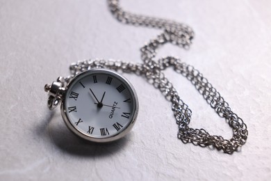 Photo of Silver pocket clock with chain on light textured table, closeup