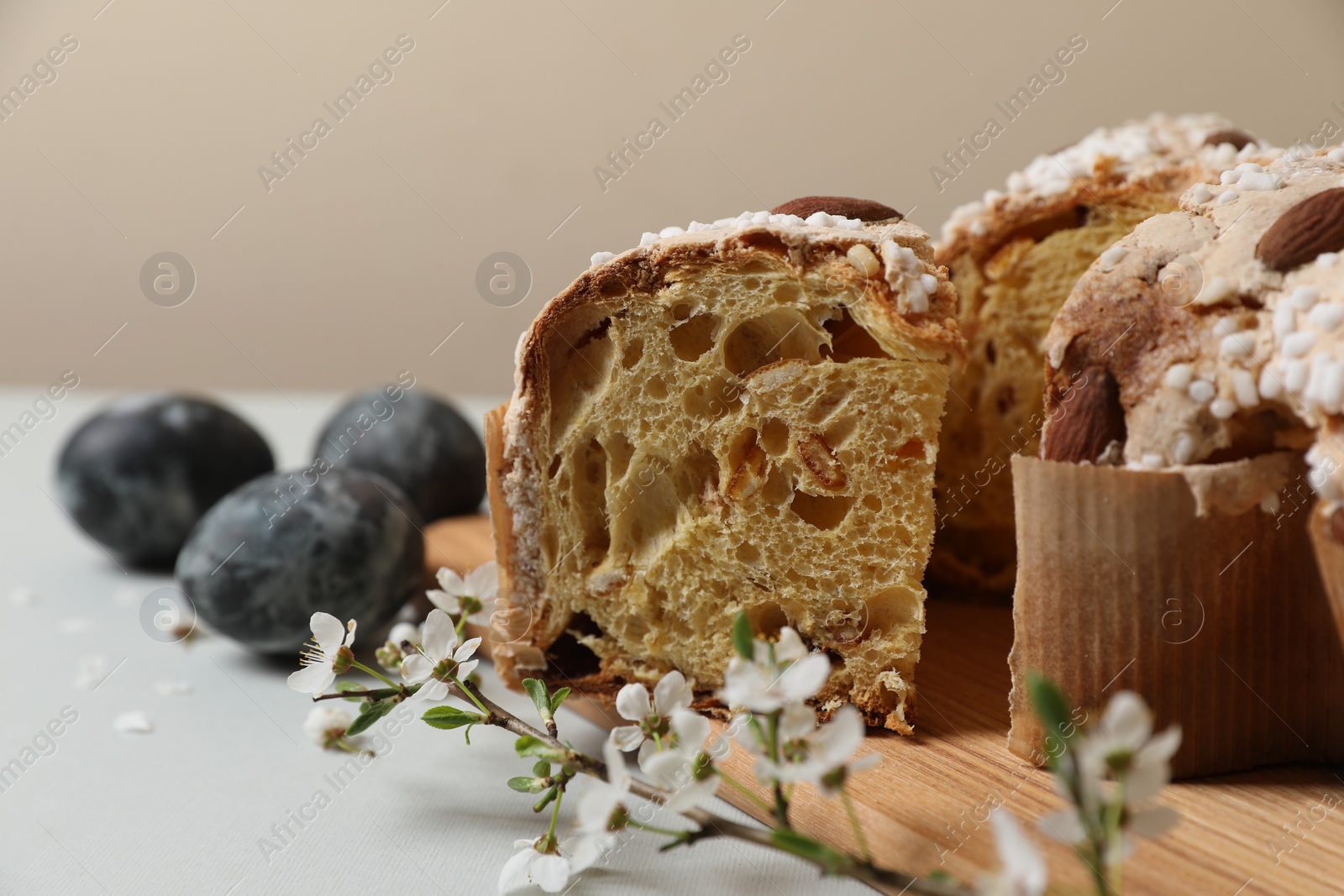 Photo of Pieces of delicious Italian Easter dove cake (traditional Colomba di Pasqua), branch with flowers and painted eggs on light grey table, closeup