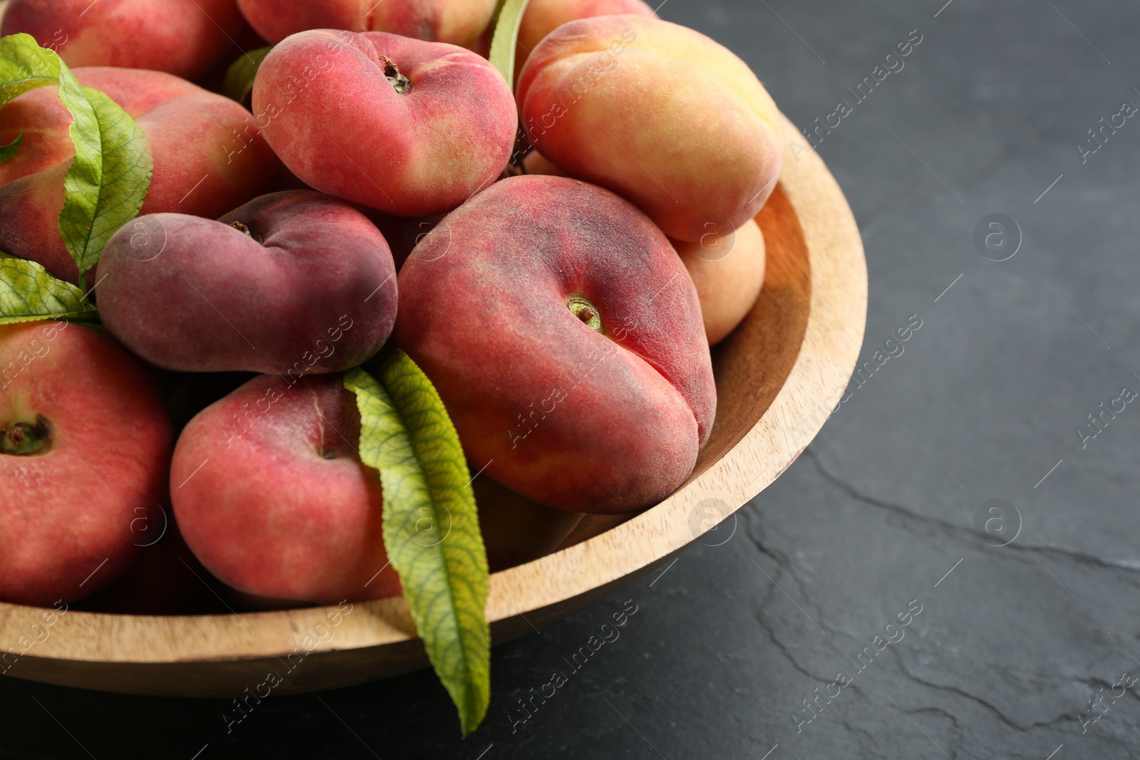 Photo of Fresh ripe donut peaches in bowl on dark table, closeup