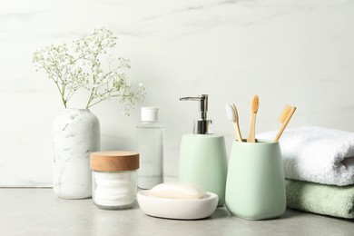 Photo of Different bath accessories, personal care products and gypsophila flowers in vase on gray table near white marble wall