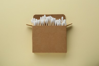 Box with wooden cotton buds on beige background, top view