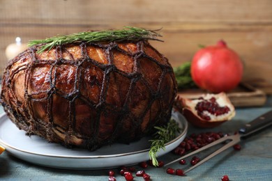 Photo of Delicious baked ham, carving fork, pomegranate seeds and rosemary on rustic wooden table, closeup