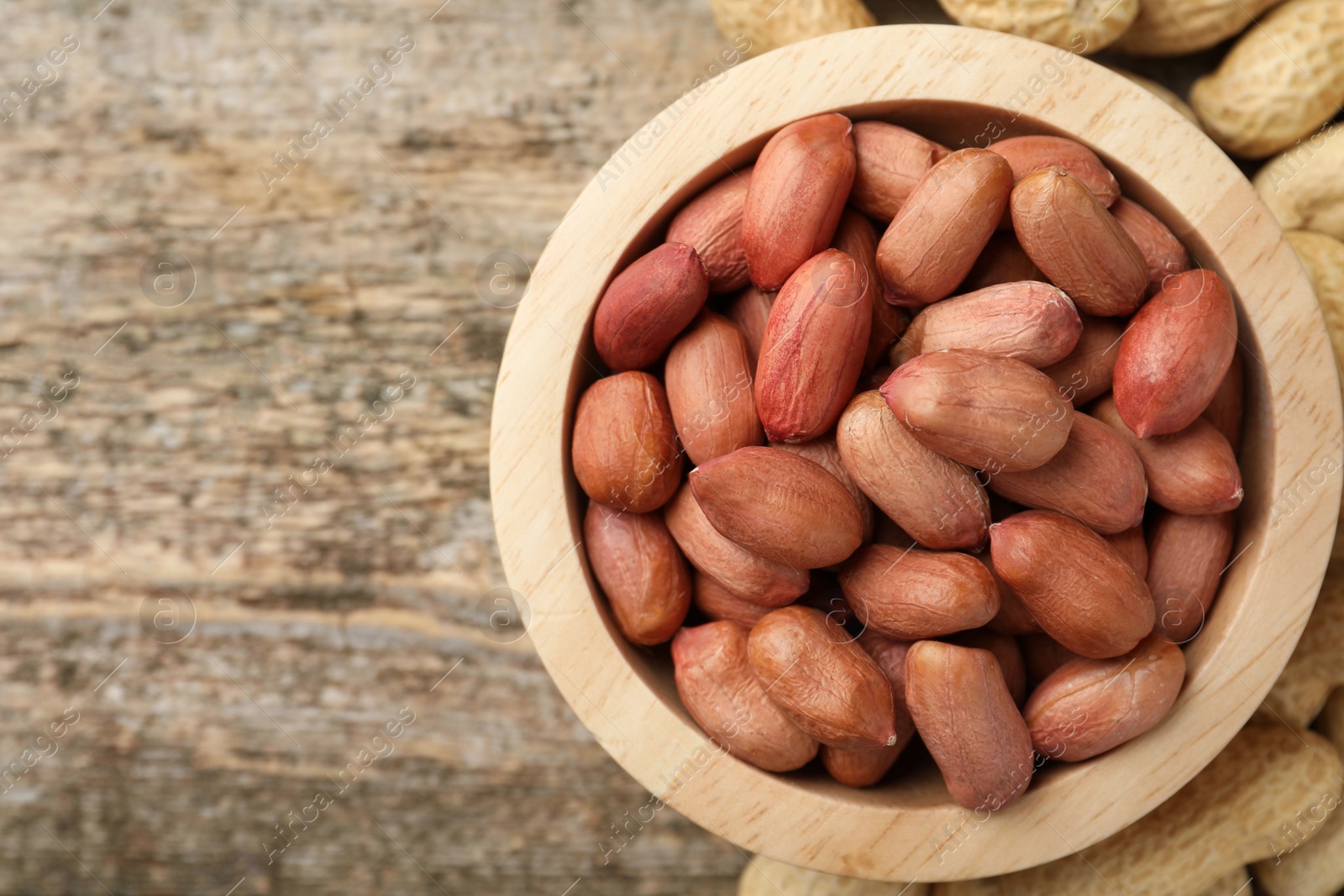 Photo of Fresh unpeeled peanuts in bowl on wooden table, top view. Space for text