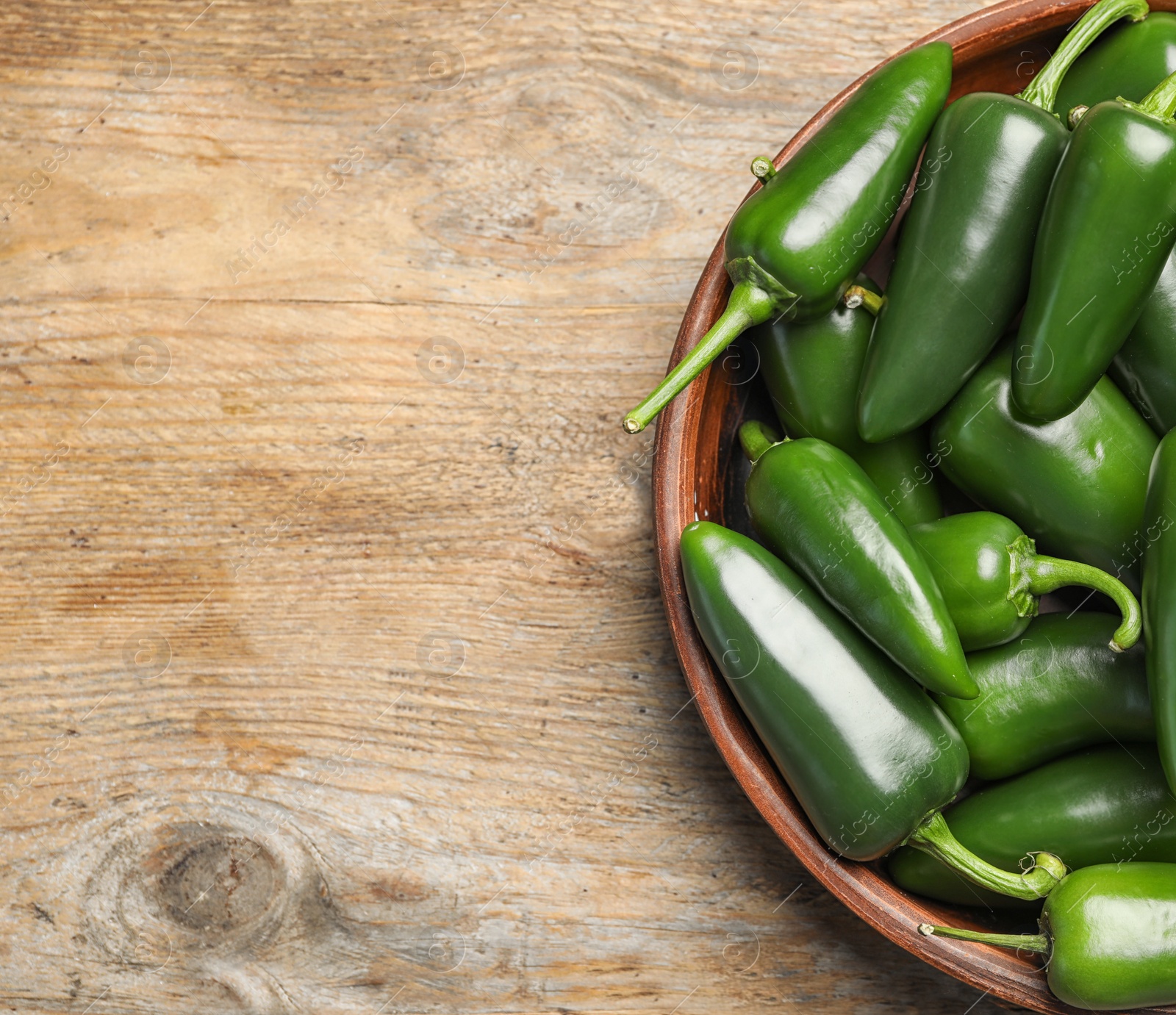 Photo of Bowl with green hot chili peppers on wooden table, top view. Space for text