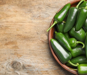 Bowl with green hot chili peppers on wooden table, top view. Space for text