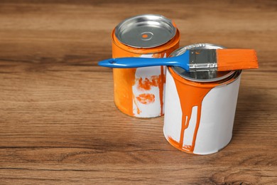 Cans of orange paint and brush on wooden table. Space for text