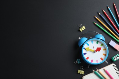 Photo of Flat lay composition with alarm clock and different stationery on black background, space for text. School time