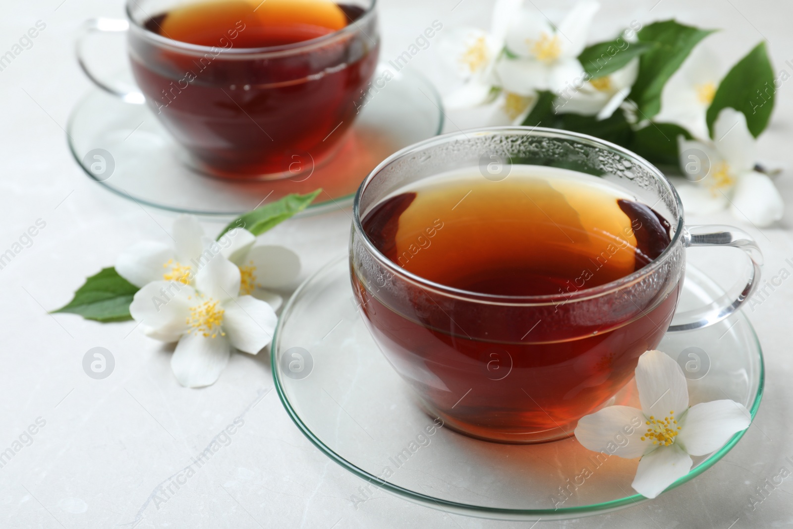 Photo of Cups of tea and fresh jasmine flowers on light grey marble table