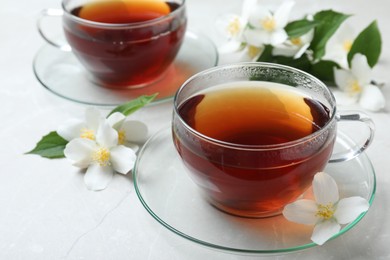 Photo of Cups of tea and fresh jasmine flowers on light grey marble table