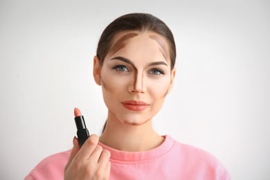 Photo of Young woman with contouring lines on her face against light background. Professional makeup products