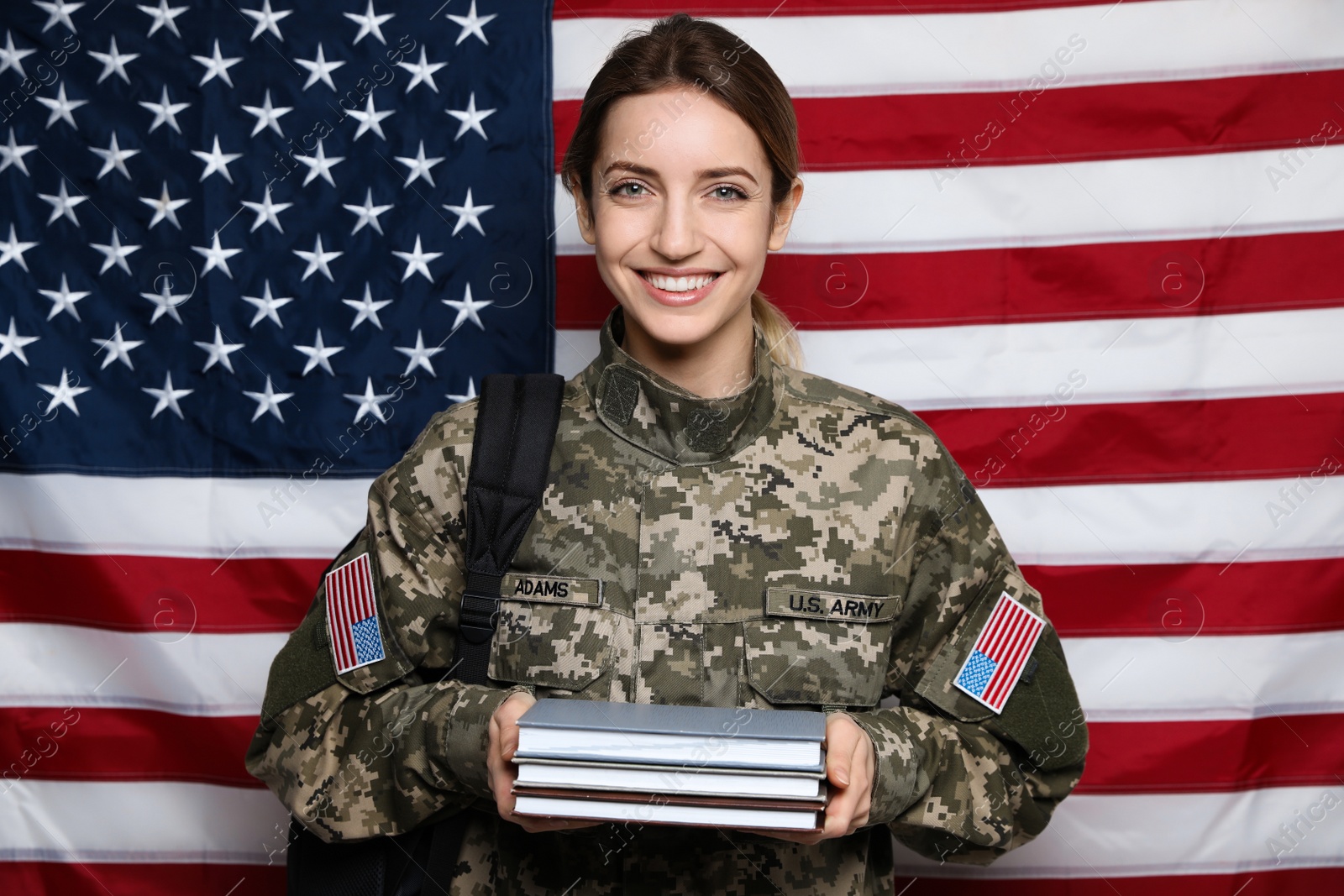 Photo of Female cadet with backpack and books against American flag. Military education