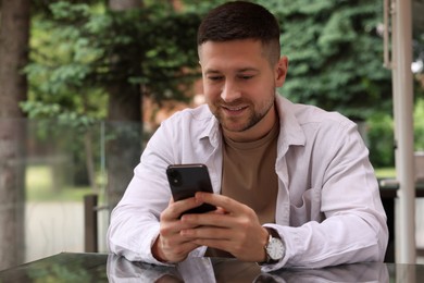 Photo of Handsome man sending message via smartphone at table in outdoor cafe