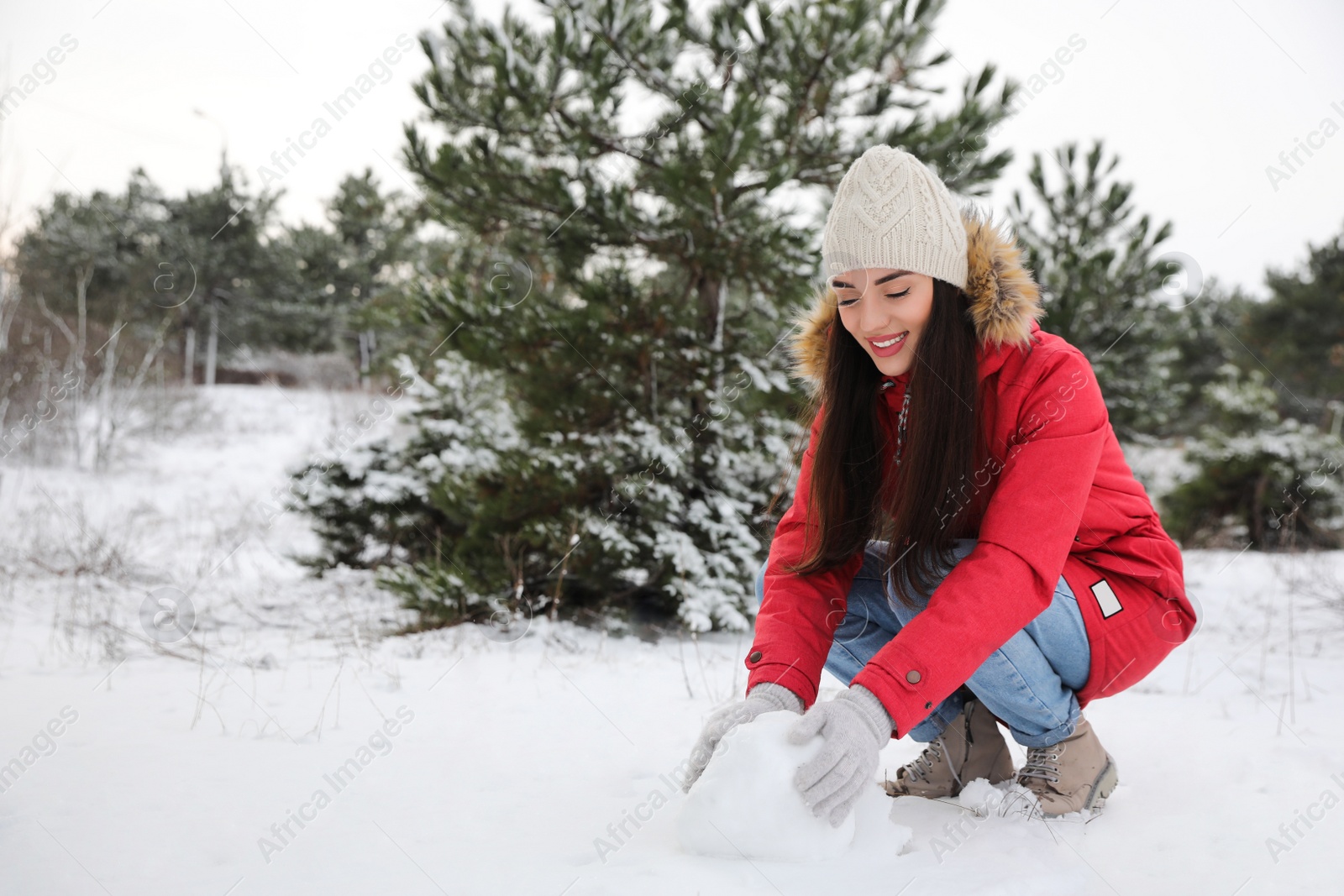 Photo of Young woman rolling snowball outdoors on winter day. Space for text