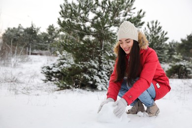 Photo of Young woman rolling snowball outdoors on winter day. Space for text