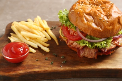 Wooden board with delicious burger, french fries and sauce on grey background, closeup