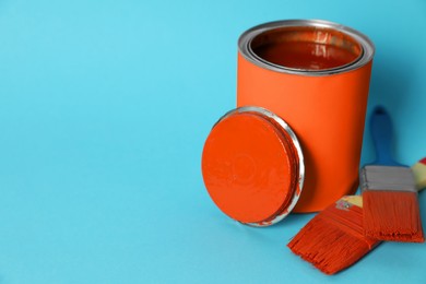 Photo of Can of orange paint and brushes on turquoise background. Space for text